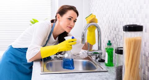 Side View Of A Happy Young Woman Cleaning Kitchen Sink