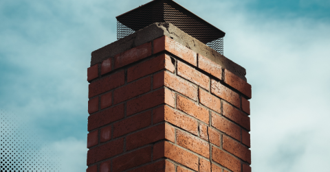 Close-up view of a brick chimney with a mesh cap against a blue sky.