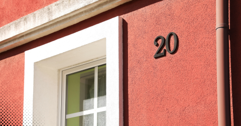 Black house number 20 on a red stucco wall beside a white window frame