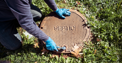 Technician opening a septic tank cover on a grassy lawn.