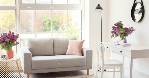 Bright living room with a gray sofa, white desk, and fresh flowers.