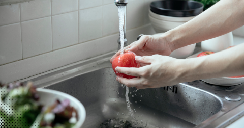 Person washing a red apple under running water in a kitchen sink.