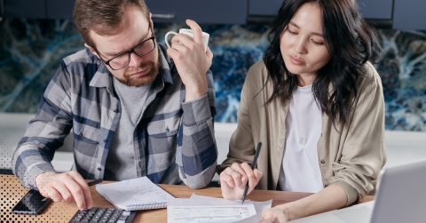 Couple reviewing financial documents and making calculations with a calculator at the table.