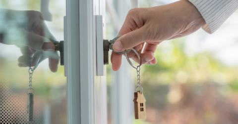 Close-up of a hand turning a key in a door lock with a wooden house-shaped keychain.