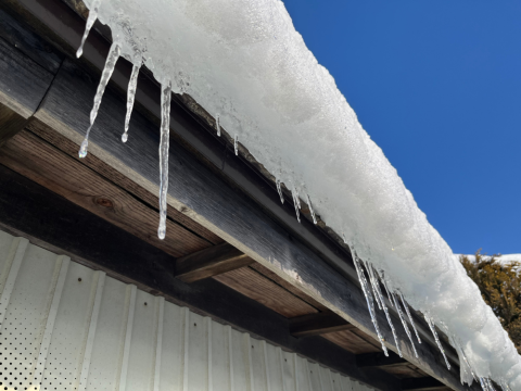 Icicles hanging from a roof under a clear blue sky.