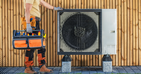 Technician standing beside an outdoor heat pump system.