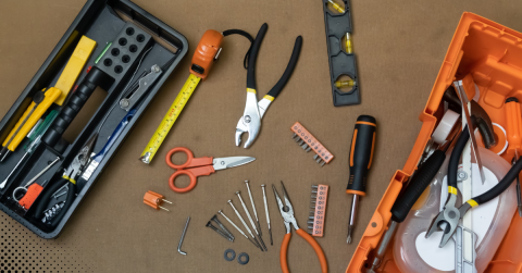 tools neatly arranged on a surface, including pliers, screwdrivers, a measuring tape, scissors, a level, and other small hardware items
